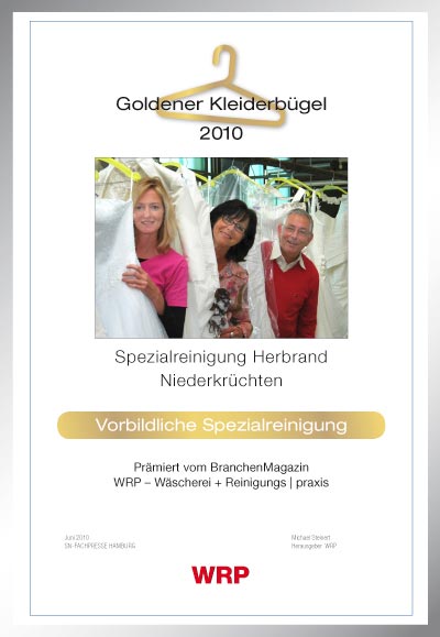 goldener Kleiderbügel verliehen an Tochter Yvonne Braun, Ursula und Axel Herbrand lächelnd zwichen gereinigten Brautkleidern